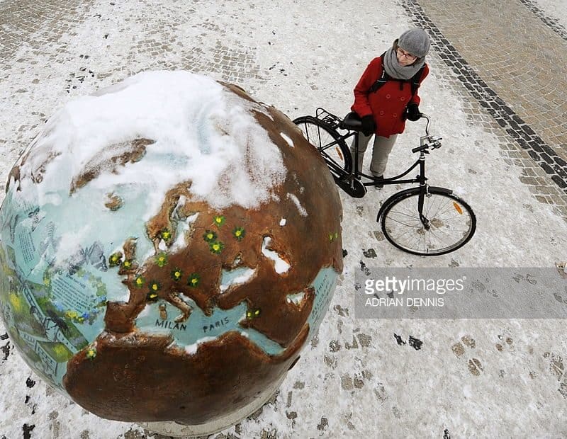 A scientist on a bicycle stands next to a globe covered in snow, exploring the impacts of climate change.