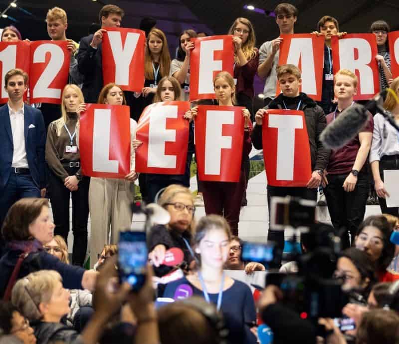 A group of people holding up signs that say 12 years left to address climate change.
