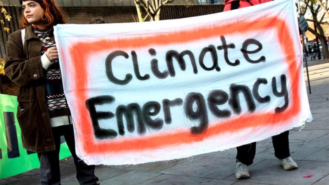 A group of people holding a sign that says climate emergency, highlighting the dangerous implications.