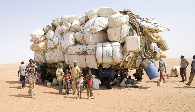 A group of people standing next to a large pile of bags amid stories of climate migration.