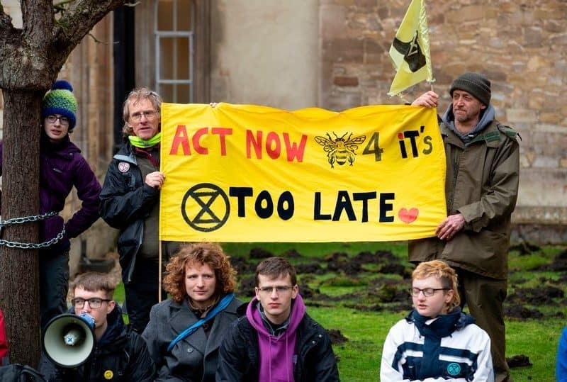 A group of people holding a sign that says act now or it's too late, demonstrating the urgent tactics of Extinction Rebellion.
