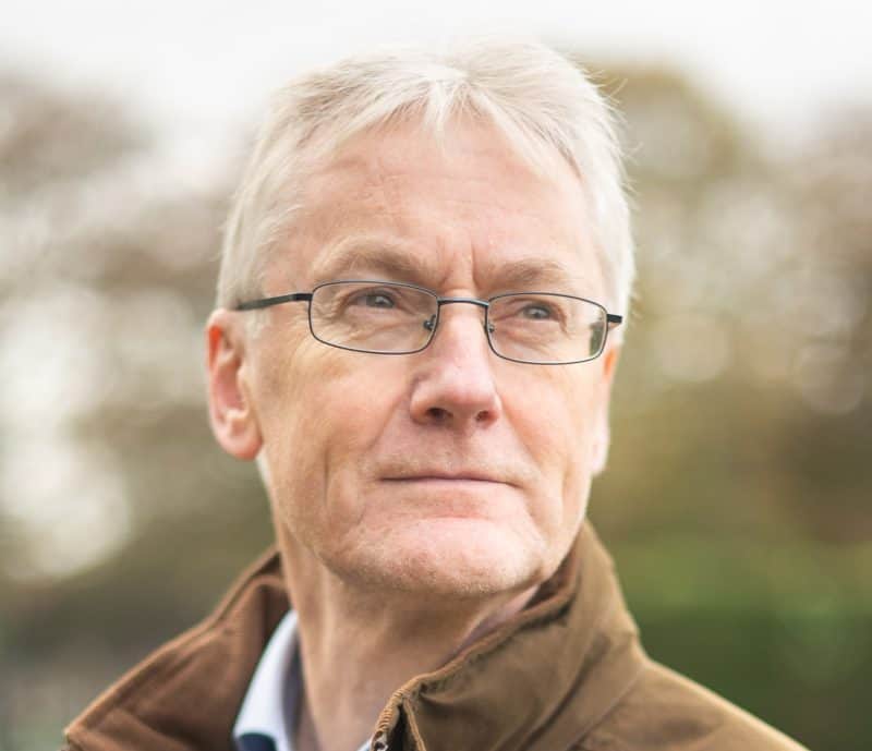 A colour portrait of Mike Julme wearing glasses and a brown jacket.