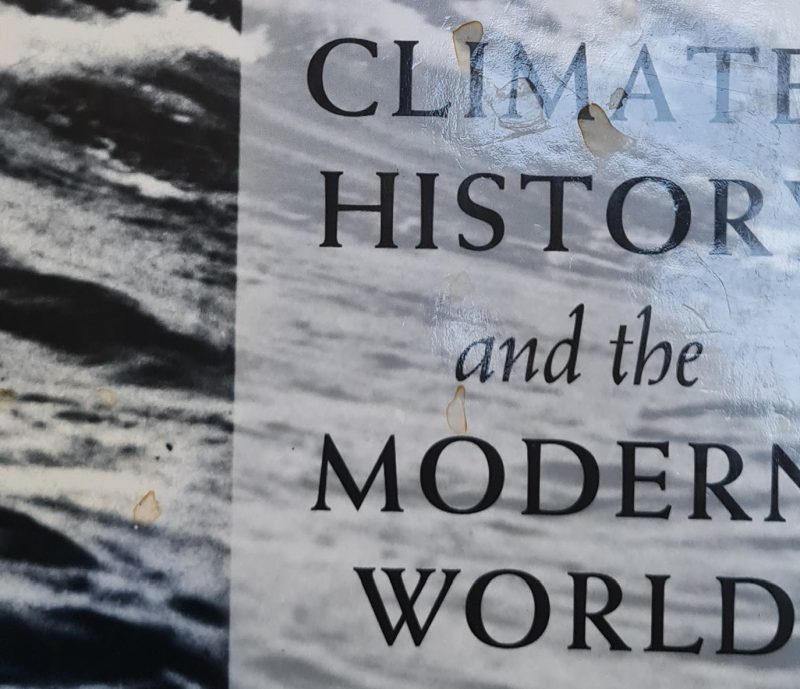 Close-up of the 1995 edition of "Climate, History and the Modern World," a climate book featuring a black and white image of turbulent water in the background.