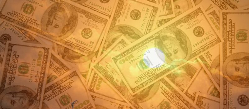 A pile of one hundred dollar bills scattered and overlaid with a warm, golden light effect.